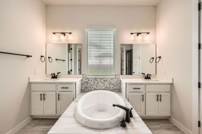 Bathroom with two vanities, a garden tub, marble look tiles, and baseboards | Image 18