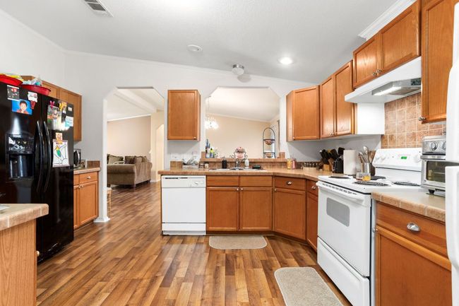 Kitchen featuring a sink, wood finished floors, under cabinet range hood, white appliances, and arched walkways | Image 15