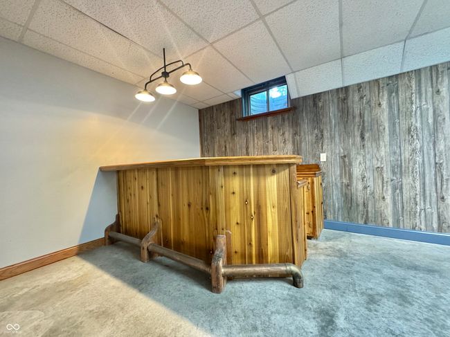 indoor dry bar with a drop ceiling, carpet flooring, wood walls, and baseboards | Image 63