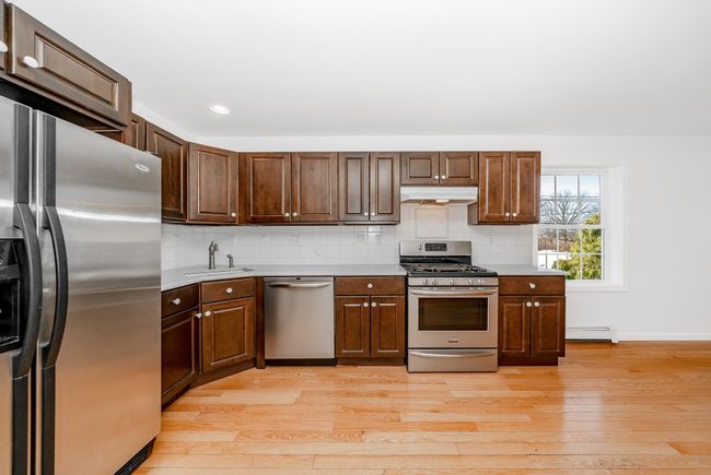Kitchen featuring a baseboard radiator, stainless steel appliances, under cabinet range hood, a sink, and backsplash | Image 5