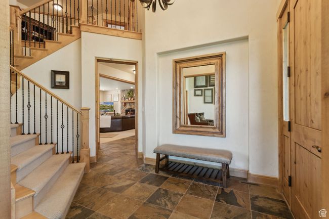 Entryway with baseboards, stone tile floors, stairs, a towering ceiling, and a stone fireplace | Image 21