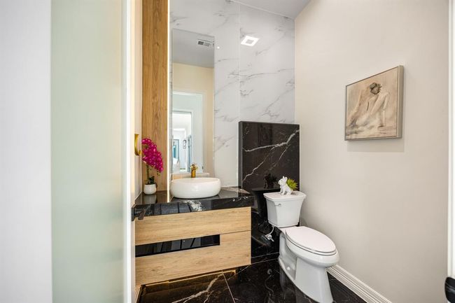 This chic half bath makes a bold statement with dramatic black marble flooring, warm wood finishes, and sleek gold accents. A vessel sink and backlit mirror add modern sophistication, while artistic touches elevate the overall ambiance—perfect for impressing guests with style and elegance. | Image 26
