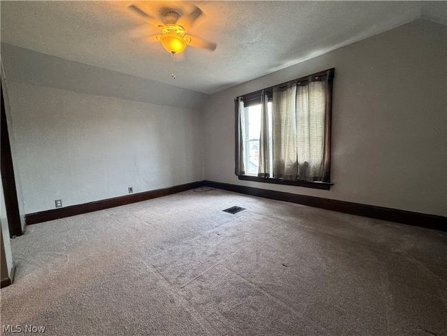 Carpeted empty room with a textured ceiling, lofted ceiling, and ceiling fan | Image 24