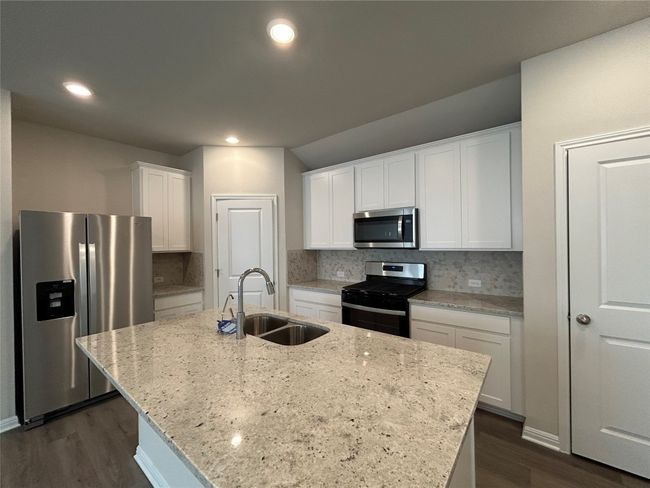 Kitchen with stainless steel appliances, dark wood-type flooring, white cabinets, tasteful backsplash, and a kitchen island with sink | Image 9