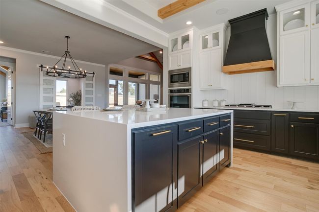 Kitchen with premium range hood, stainless steel appliances, beam ceiling, white cabinets, and a center island | Image 14