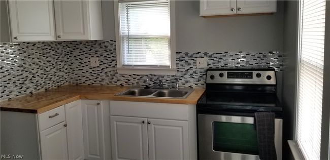 Kitchen featuring backsplash, sink, electric range, and white cabinets | Image 3