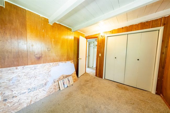 Unfurnished bedroom with carpet, wooden walls, and a closet | Image 12
