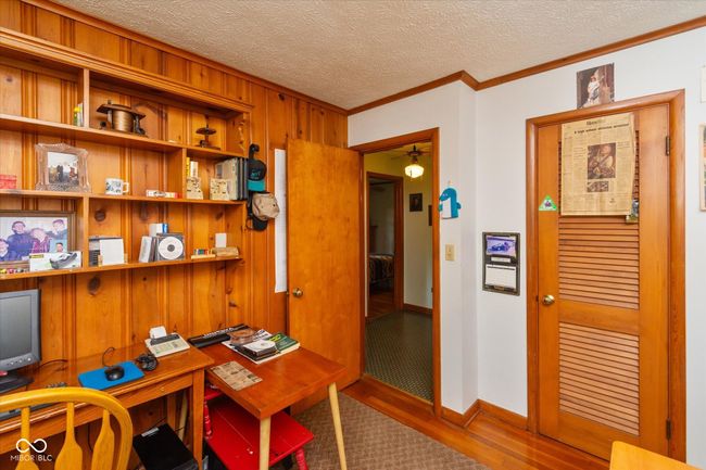 office space featuring ornamental molding, wood finished floors, wooden walls, a textured ceiling, and a ceiling fan | Image 20