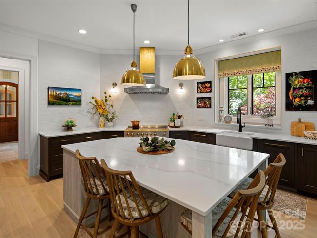 Generously sized quartz top kitchen island can seat four and provides storage. Note Frame TV above cabinets on left side. Lighting updates include pendants over the island and flanking the La Cornue Hood. Shaws Original cast iron apron sink and ASKO dish washer to the right of the sink. | Image 14