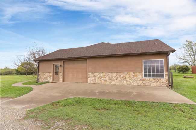 View of side of property with a shingled roof, a garage, stone siding, and a lawn | Image 4