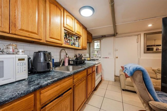 Kitchen with dark stone counters, light tile patterned flooring, white appliances, sink, and backsplash | Image 13