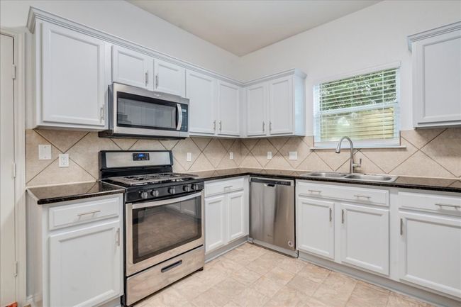 The kitchen boasts freshly repainted cabinets with new hardware, granite countertops, a combination of stainless and black appliances, and a walk-in pantry including a new faux wood blind in kitchen window. | Image 7