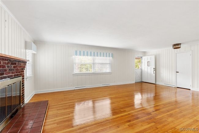Unfurnished living room with visible vents, a baseboard heating unit, baseboards, light wood finished floors, and a brick fireplace | Image 10
