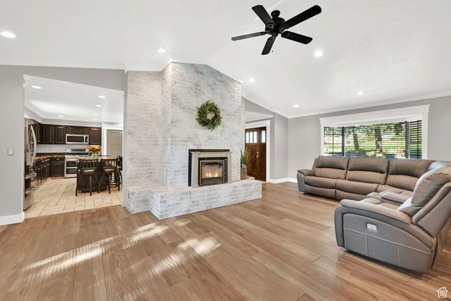 Living room with vaulted ceiling, a fireplace, light wood-type flooring, crown molding, and ceiling fan | Image 10