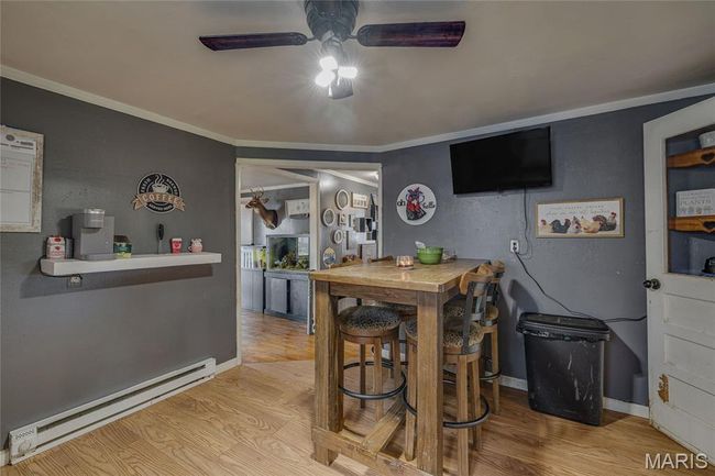 Bar area with baseboard heating, a ceiling fan, wood finished floors, crown molding, and baseboards | Image 12