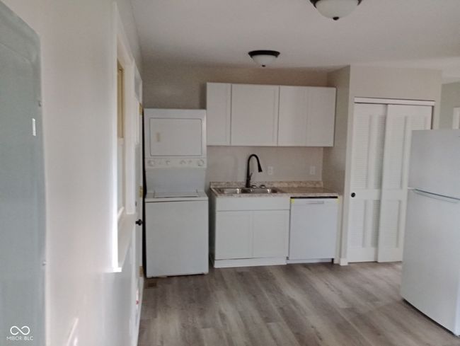 kitchen with stacked washer / drying machine, light wood finished floors, a sink, and white appliances | Image 7