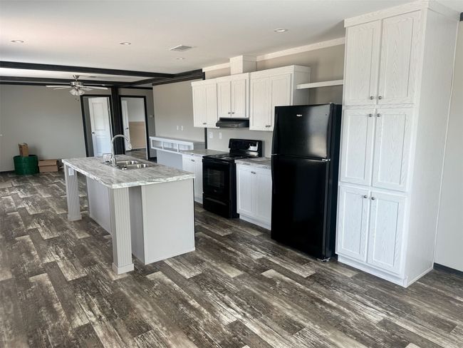 Kitchen with dark wood-type flooring, a sink, ceiling fan, white cabinets, and black appliances | Image 7