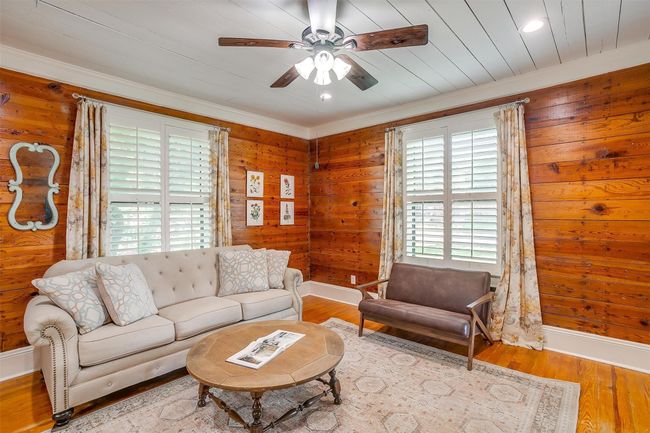 Living room with a ceiling fan, wood finished floors, wood walls, and crown molding | Image 13