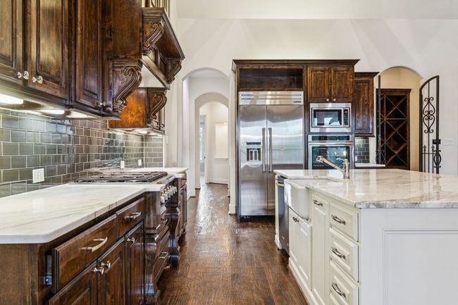 Gourmet kitchen with built in appliances, gas cooktop, huge island with breakfast bar, wine cellar, dark wood-style floors, and backsplash | Image 9