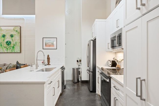 Kitchen with appliances with stainless steel finishes, white cabinets, concrete floors, and decorative backsplash | Image 10