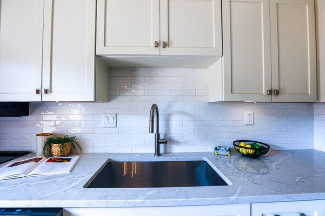 Kitchen with backsplash, light stone quartz counters, and white cabinetry. | Image 9
