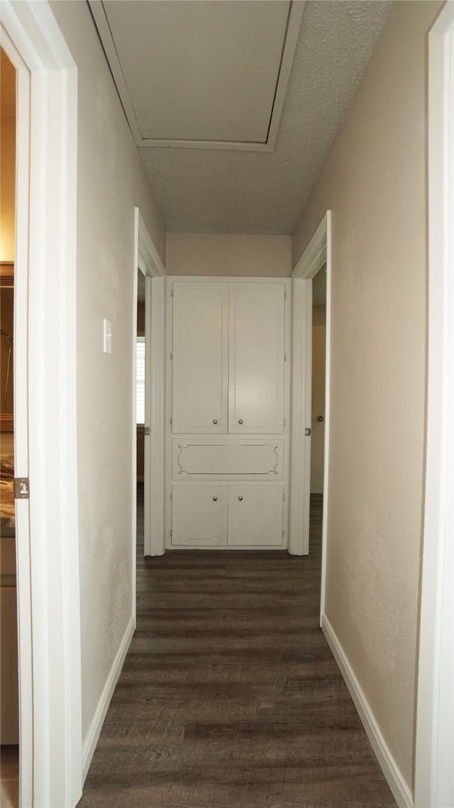 The hallway takes you to the bedrooms, guest bath, and the built-in storage cabinet with a laundry drop | Image 11