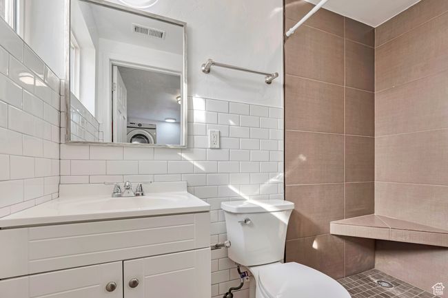 Bathroom with visible vents, toilet, vanity, tile walls, and a shower | Image 13
