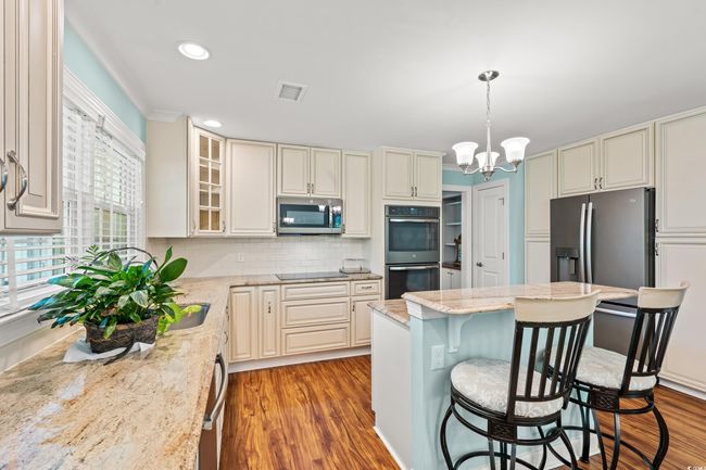 Kitchen featuring appliances with stainless steel finishes, wood finished floors, a breakfast bar area, light stone counters, and tasteful backsplash | Image 6