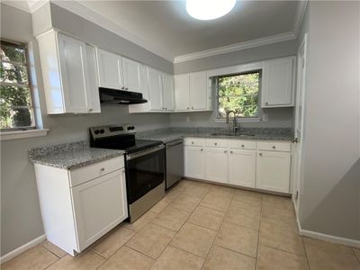 Kitchen with light stone countertops, sink, white cabinetry, stainless steel appliances, and ornamental molding | Image 2