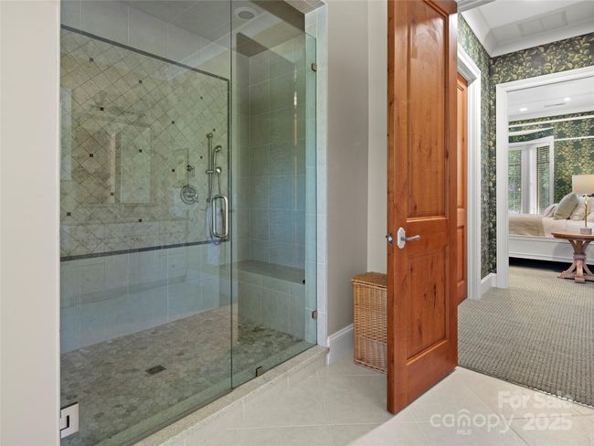 Primary bath walk-in shower with four body sprays and bench. Two separate walk-in closets are accessed between the primary bath and bedroom. | Image 24