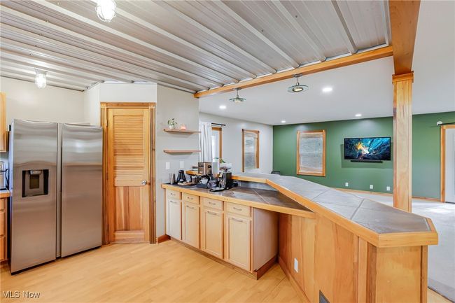 Kitchen with stainless steel fridge with ice dispenser, tile countertops, light wood finished floors, a peninsula, and recessed lighting | Image 14