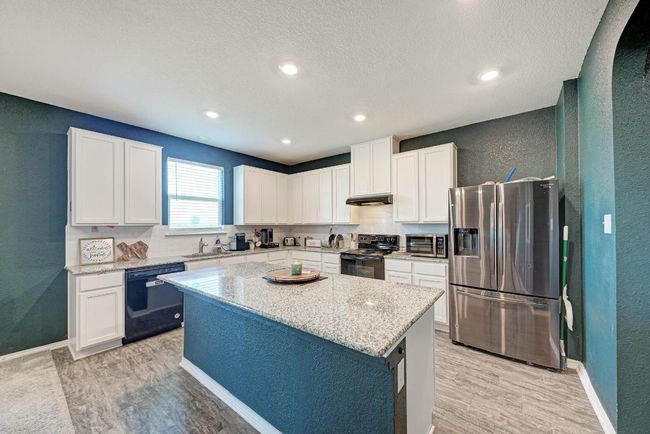 Kitchen featuring black appliances, a textured wall, under cabinet range hood, a center island, and white cabinetry | Image 16