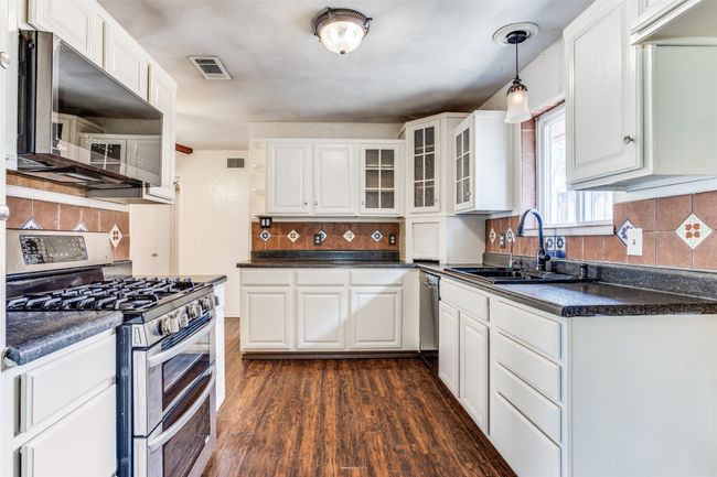Kitchen with appliances with stainless steel finishes, a sink, dark countertops, white cabinets, and decorative backsplash | Image 12