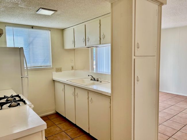 Kitchen featuring light tile patterned flooring, white appliances, light countertops, a textured ceiling, and a sink | Image 5