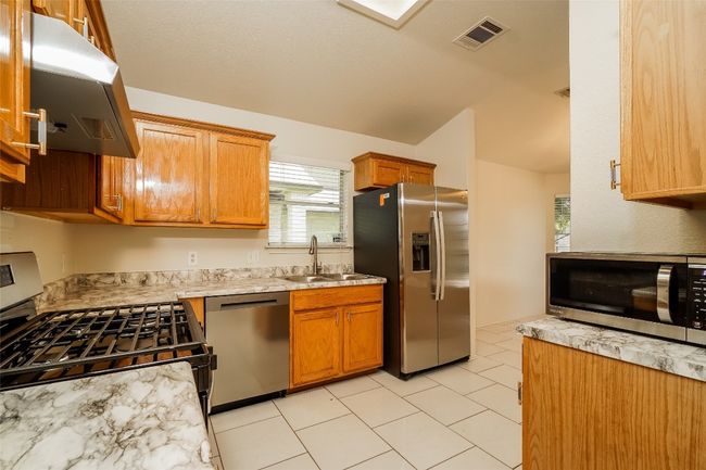 Kitchen featuring stainless steel appliances, ventilation hood, lofted ceiling, light tile patterned flooring, and brown cabinets | Image 11