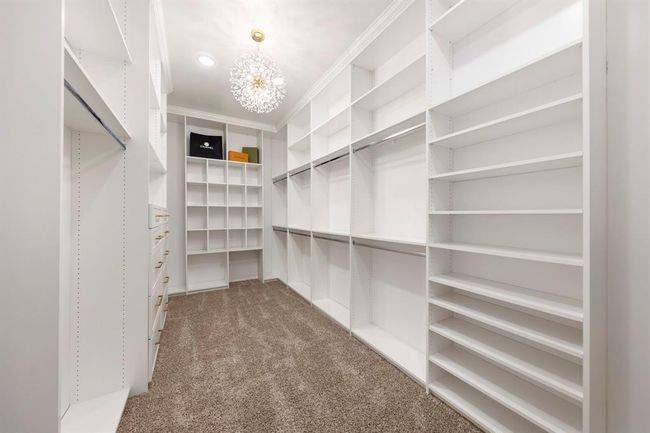 This expansive walk-in closet features a custom organization system with endless shelving, soft-close drawers, double hanging space, and a glamorous chandelier that turns daily routines into a boutique-like experience. | Image 25