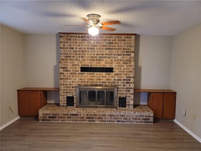 Unfurnished living room with a ceiling fan, wood finished floors, a brick fireplace, and a textured ceiling | Image 5