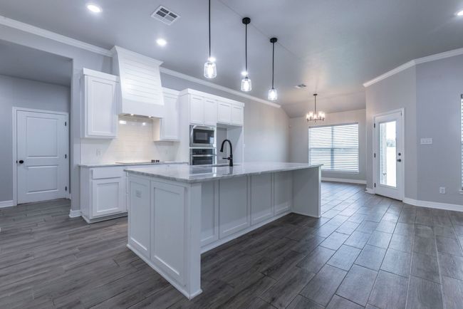 Kitchen featuring stainless steel appliances, ornamental molding, premium range hood, white cabinets, and a chandelier | Image 7