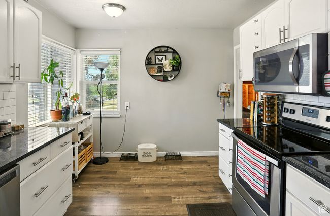 Kitchen with stainless steel appliances, dark wood-style flooring, tasteful backsplash, and white cabinets | Image 10