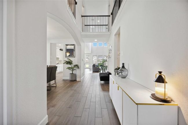 This photo showcases a modern, open-concept home interior with high ceilings and abundant natural light. The space features elegant wood flooring, a sleek hallway with contemporary decor, and a view into a spacious living area, ideal for comfortable living and entertaining. | Image 4