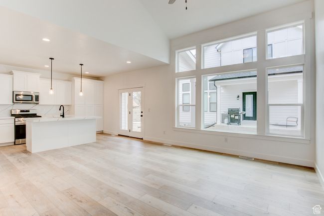Unfurnished living room with a sink, high vaulted ceiling, light wood-style flooring, baseboards, and visible vents | Image 4