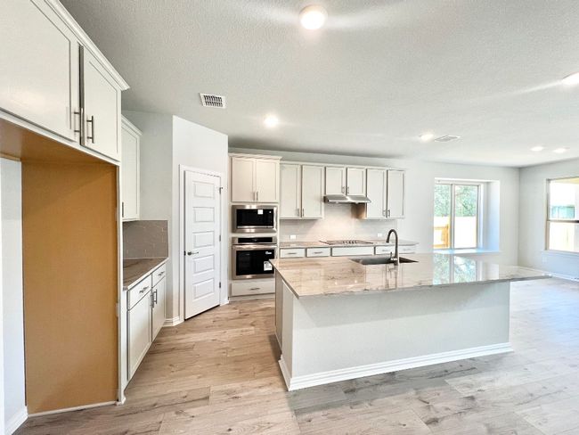 Kitchen featuring light stone counters, backsplash, stainless steel appliances, a kitchen island with sink, and a textured ceiling | Image 4