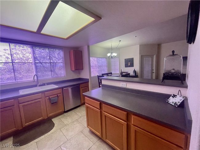 Kitchen featuring an inviting chandelier, dishwasher, a sink, dark countertops, and a peninsula | Image 6