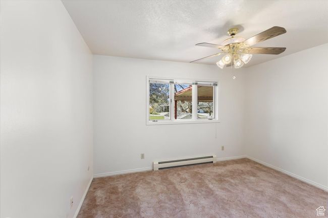 Carpeted empty room with a baseboard heating unit, ceiling fan, and baseboards | Image 16