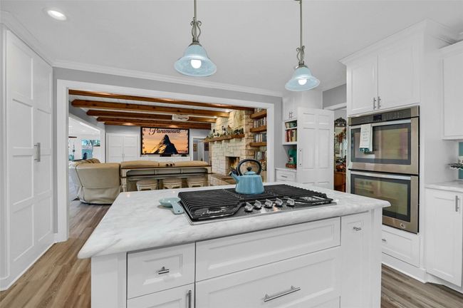 Kitchen with stainless steel appliances, light wood-style flooring, a fireplace, white cabinetry, and ornamental molding | Image 14