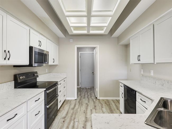 Kitchen featuring light stone counters, double oven range, black dishwasher, white cabinetry, and stainless steel microwave | Image 11