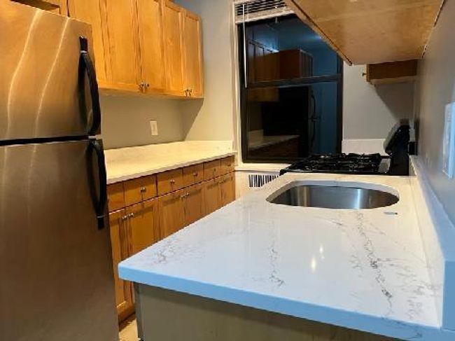 Kitchen featuring light stone countertops, freestanding refrigerator, brown cabinets, and range with gas stovetop | Image 25