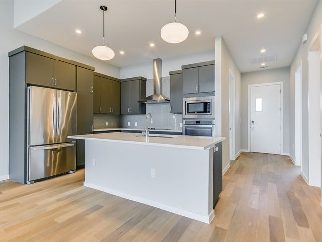 The modern kitchen features quartz counters, like-new stainless appliances, vent hood, and includes the fridge! | Image 6