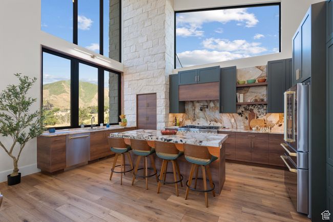 Kitchen with appliances with stainless steel finishes, light wood finished floors, a kitchen island, a kitchen breakfast bar, and a high ceiling | Image 25