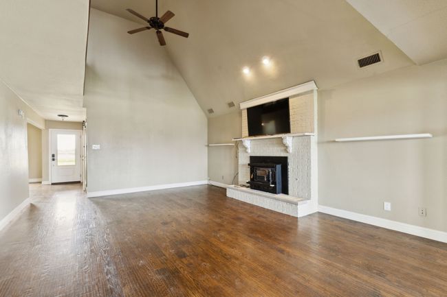 Unfurnished living room with baseboards, visible vents, high vaulted ceiling, ceiling fan, and hardwood / wood-style flooring | Image 9